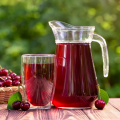 Dark red koolaid in glass pitcher and cup on outside table