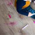 Toddler holding marker sitting on wooden floor, pink marker scribbles on floor